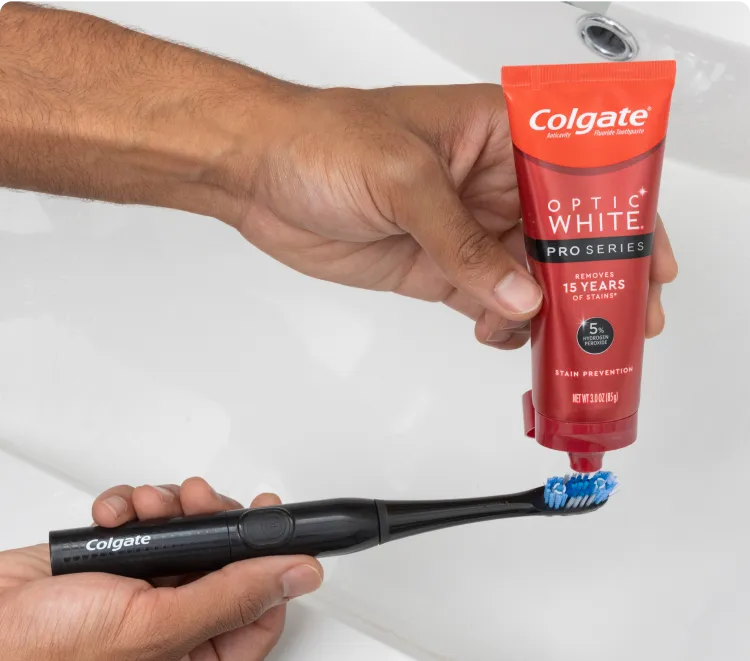 A person putting Optic White Pro Series Whitening Toothpaste on an Optic White Pro Series Powered Toothbrush