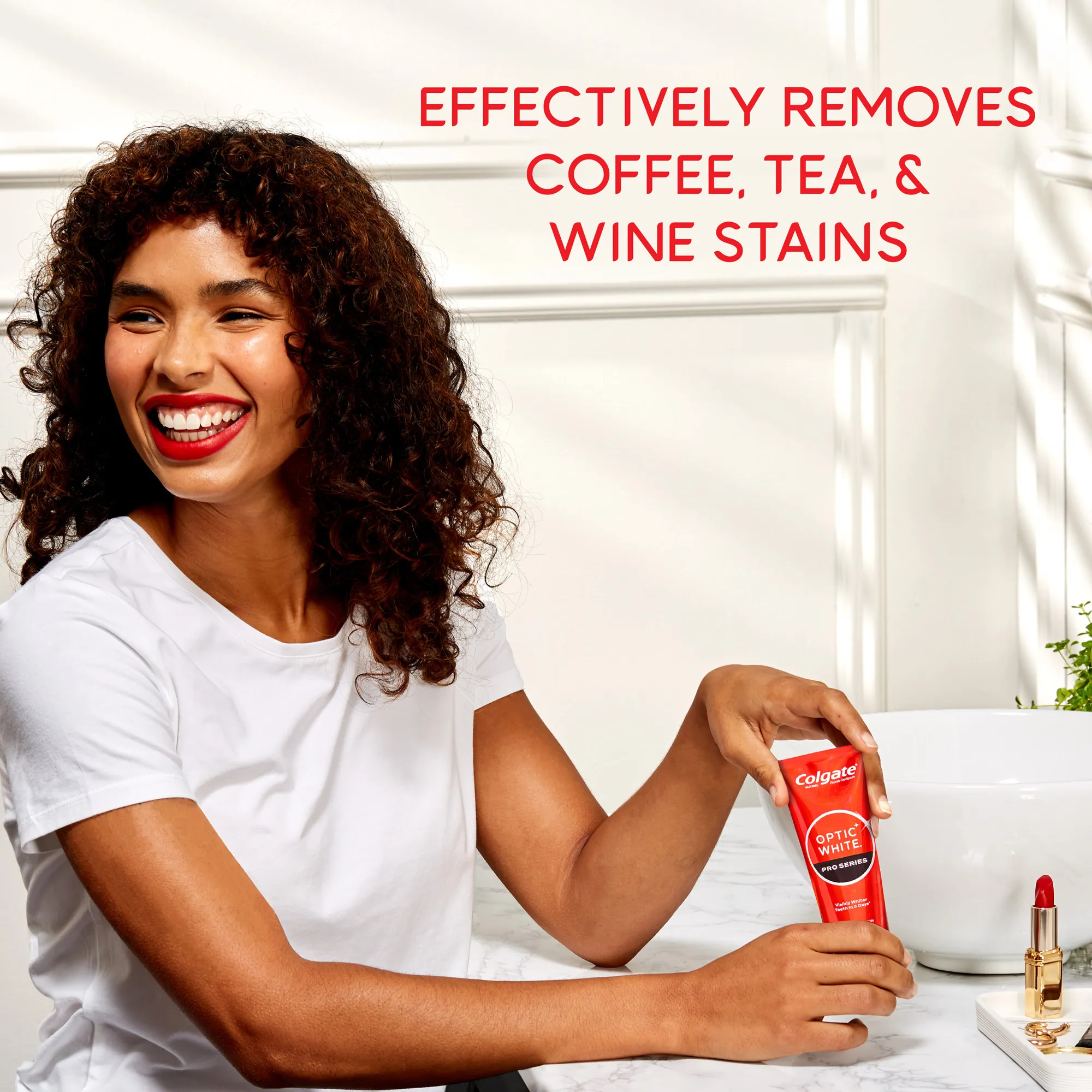 A woman smiling while holding a tube of Colgate Optic White Pro Series Stain Prevention Whitening Toothpaste. In text: Effectively removes coffee, tea & wine stains.