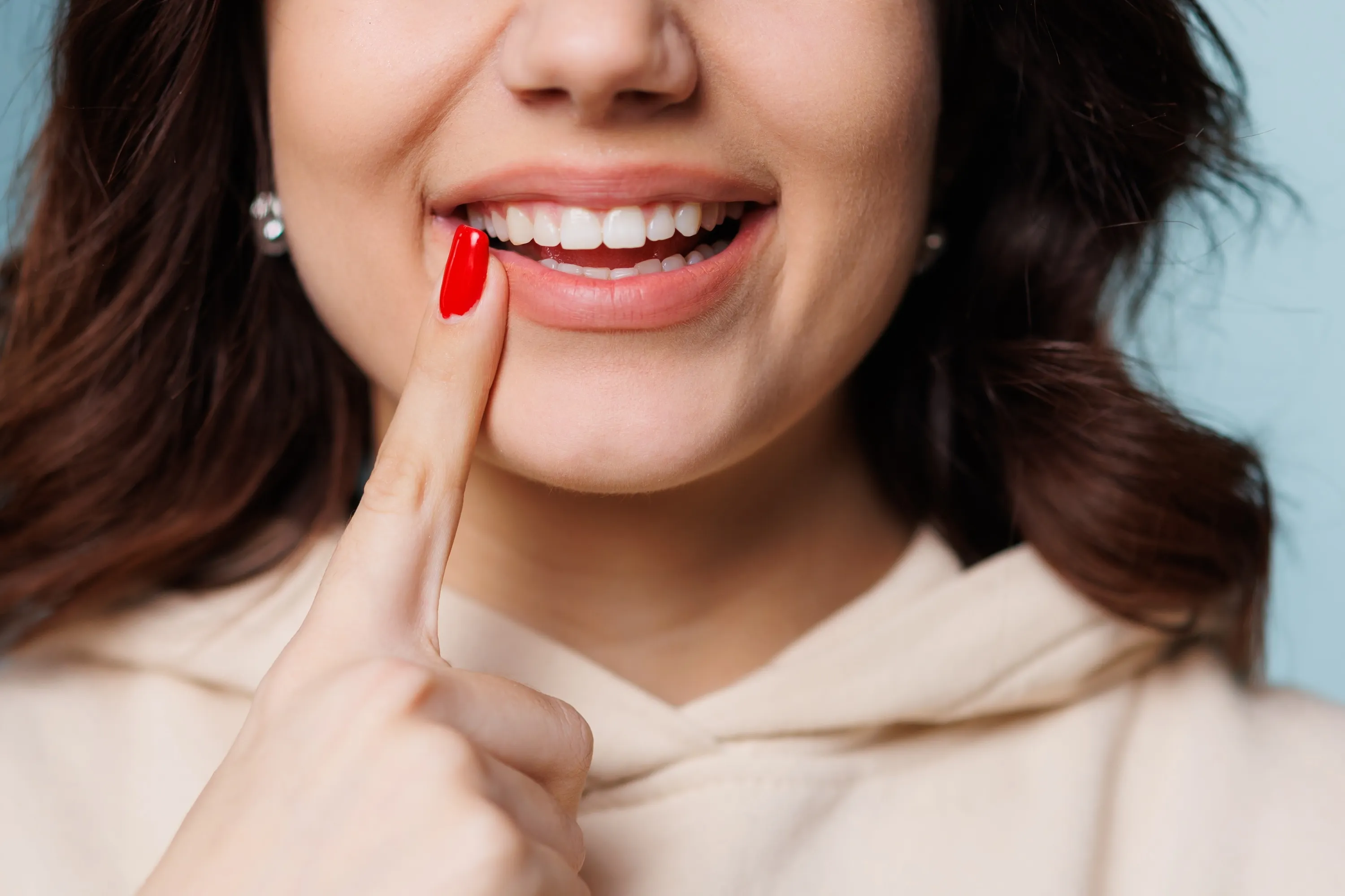 Happy girl showing toothy smile, pointing finger at healthy white teeth. Clinic patient satisfied with dentist service, enamel cleaning, whitening, dental care, correction. Cropped shot, close up