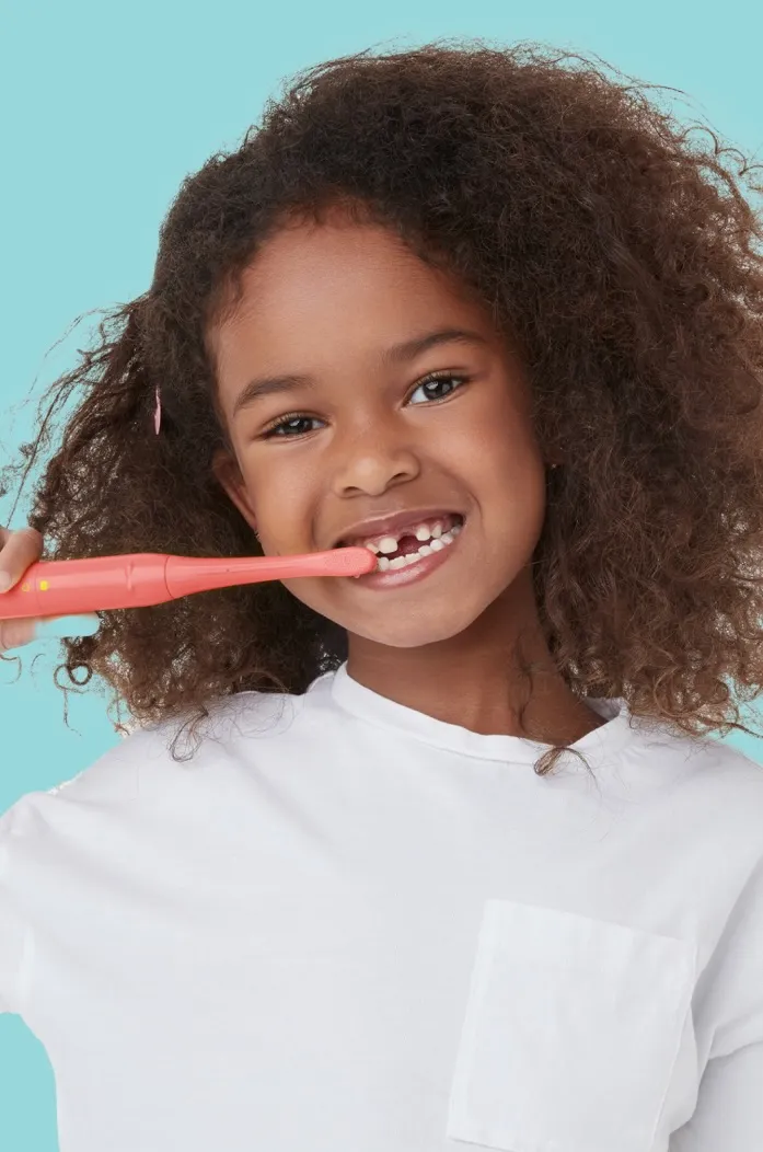 girl holding colgate hum smart battery powered coral red toothbrush for kids