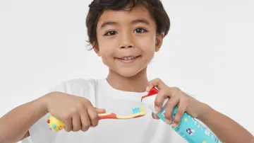 boy smiling while applying colgate mild bubble fruit kids toothpaste onto colgate hum smart manual yellow toothbrush for kids
