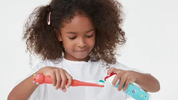 girl applying colgate mild bubble fruit kids toothpaste on colgate hum smart battery powered coral red toothbrush for kids