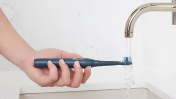 hand holding colgate hum adult smart rhythm sonic toothbrush rinsing brush head on the sink