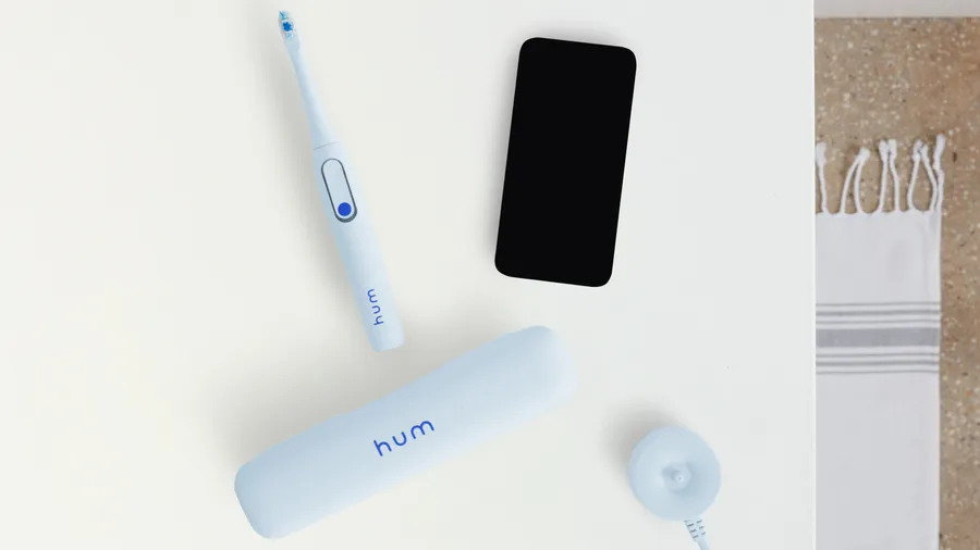 blue colgate hum adult smart electric toothbrush, case, charging dock, and a smartphone