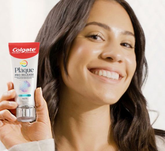 woman smiling and holding Colgate Total Plaque Pro-Release Fresh Mint Toothpaste tube
