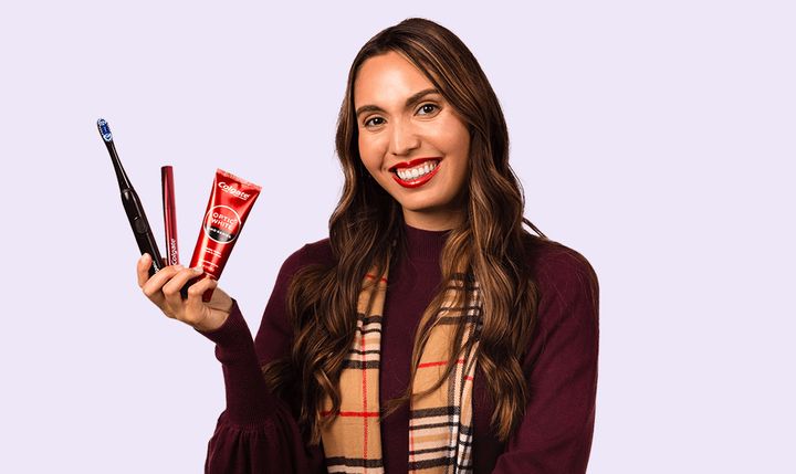 A woman smiling while holding the items in the Optic White Bundle (Optic White Pro Series Powered Toothbrush, Optic White Overnight Teeth Whitening Pen, Optic White Pro Series Whitening Toothpaste).