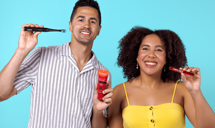 A man wearing a striped shirt holding a Colgate Optic White Pro Series Powered Toothbrush and a woman in a yellow shirt holding an Optic White Overnight Teeth Whitening Pen.