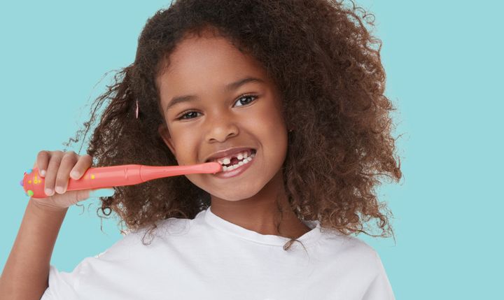 girl holding colgate hum smart battery powered coral red toothbrush for kids