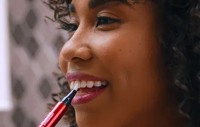 Woman using the optic white teeth whitening pen on her teeth